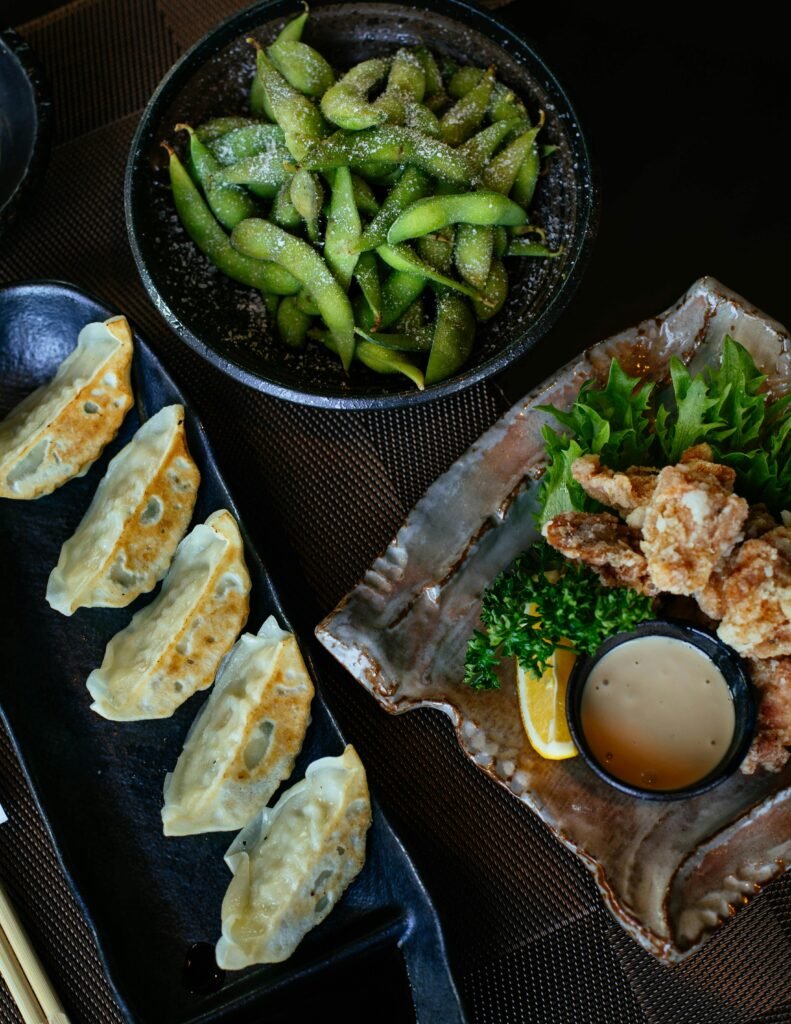 Top view of Japanese cuisine with dumplings, fried chicken, and edamame in a restaurant setting.