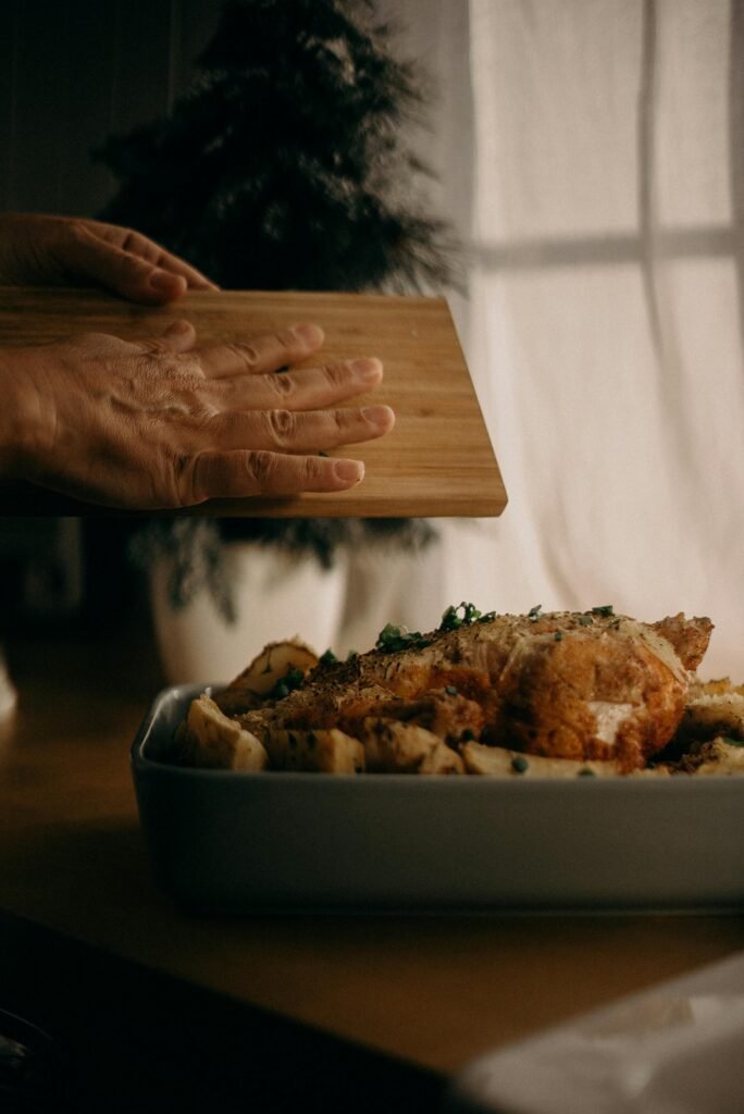 Hands sprinkling herbs over delicious roast chicken and potatoes indoors.