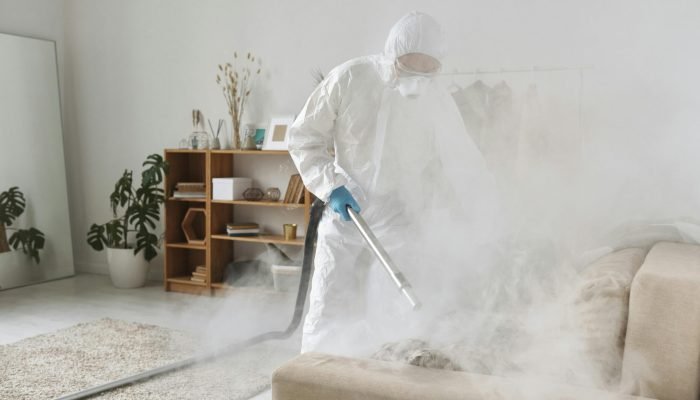 A person in PPE fumigates a living room for disinfection, ensuring safe environment.